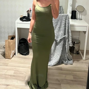 Grön långklänning med smala axelband - Elegant grön långklänning med smala axelband och figurnära passform. Perfekt för en festlig kväll med sin stilrena design och mjuka material.