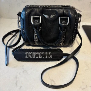  Zadig & Voltaire väska nano - INTRESSEKOLL en snygg svart axelväska i skinn från Zadig & Voltaire. Väskan har coola silverdetaljer och en justerbar axelrem med logotyp. Perfekt för en rockig look! 🖤den har tappat lite färg på dragkedjan (se bild 2&3) NANO XS