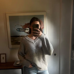 Grå stickad tröja från Ginatricot - Säljer en mysig grå stickad tröja från Ginatricot. Tröjan har en v-ringad design och långa ärmar, perfekt för kyligare dagar. Den har en avslappnad passform som gör den bekväm att bära. Perfekt för en stilren och enkel look.