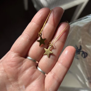 Guldstjärna örhängen - Snygga örhängen i guld med stjärnformade hängen. Perfekta för att ge en touch av glamour till din outfit. De har en enkel och elegant design som passar till många tillfällen.