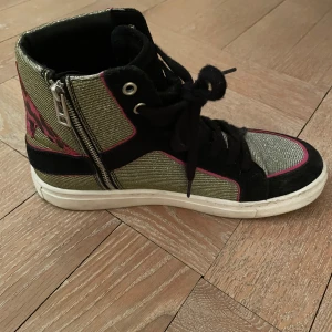Höga Zadig voltaire sneakers med dragkedja och snörning - Snygga höga sneakers i en mix av svart mocka och guld med rosa detaljer. Skorna har både snörning och dragkedja för enkel på- och avtagning. Perfekta för en trendig look. Nypris 1900 säljer för 900, änvända fåtals gånger och är i väldigt bra skick
