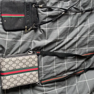 Axelväskor med monogrammönster - Två stilrena axelväskor med monogrammönster och klassiska ränder i grönt och rött. Den ena är i grått med svart mönster och den andra i svart. Båda har dragkedja och justerbara axelremmar.