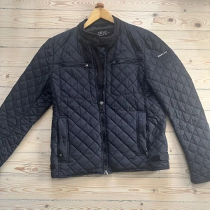 Svart quiltad jacka från Replay - Snygg svart quiltad jacka från Replay med dragkedja och flera praktiska fickor. Jackan har en stilren design med långa ärmar och en hög krage. Perfekt för kyligare dagar.