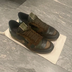 Camouflage sneakers från Valentino - Snygga sneakers i camouflagefärger från Valentino. Skorna har en kombination av gröna och bruna nyanser med svarta detaljer. De har snörning och en unik design med en mönstrad sula. Perfekta för en stilren och modern look. Skicket är bra och de är självklart äkta. För fler frågor eller bilder kom privat. Priset är ej hugget i sten!