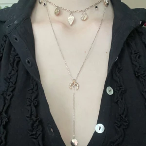 Halsband med berlocker i guld - Säljer ett trendigt lager-på-lager halsband i guld med flera berlocker, bland annat hjärta, måne och runda mynt. Kedjan är tunn och elegant, perfekt för att ge en cool touch till din outfit.