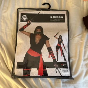 Svart ninja kostym  - Cool svart ninja kostym med röda band och tillbehör. Inkluderar topp, byxor, bälte och armvärmare. Perfekt för maskerad eller temafest. Mask och röda detaljer ger en tuff look.