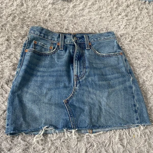 Jeanskjol från Levi's - Säljer en klassisk blå jeanskjol från Levi's med rå kant nertill och femficksmodell. Kjolen har bälteshällor, knapp- och dragkedjestängning samt tydliga sömmar och bakfickor med Levi's-logga. Väldigt fin och gullig. S/xs