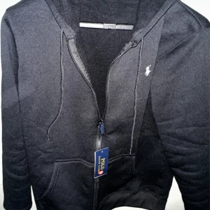 Svart hoodie med dragkedja från Ralph Lauren , HELT NY  - Klassisk svart hoodie från Ralph Lauren med dragkedja framtill och vit broderad logga på bröstet. Tröjan har huva med snörning HELT NY  Använd 2 gånger , säljs billigt 