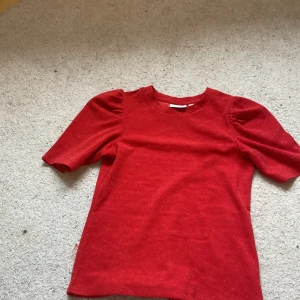 Röd glittrig topp från Kappahl - Säljer en röd glittrig topp från Kappahl i storlek XS. Toppen har korta puffärmar och rund halsringning. Perfekt för dig som vill sticka ut lite extra med ett glittrigt plagg! Den har en liten defekt vid magen då en tråd har åkt av men inget som syns super mycket, säljer då den aldrig kommer till användning❤️🙌🏻