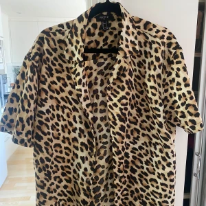 Leopardmönstrad skjorta från Forever 21 - Säljer en kortärmad skjorta från Forever 21 med leopardmönster i beige, brunt och svart. Skjortan har klassisk krage och knäppning framtill. Perfekt för dig som vill sticka ut med en djärv stil.