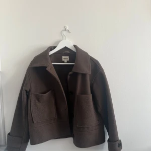 Brun jacka från Kappahl  - Säljer en brun jacka från Kappahl med stora fickor framtill och knappar. Jackan har klassisk krage, lång ärm med knappdetalj vid ärmslut och boxig passform. Perfekt för lager-på-lager under kyliga dagar.