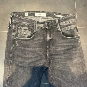Svarta Replay Anbass jeans - Säljer ett par svarta Replay Anbass jeans med snyggt tvättad look. Klassisk femficksmodell med normal passform och raka ben. Jeansen har diskreta slitningar och tydliga sömmar. Perfekta för dig som gillar stilrena och bekväma jeans. Storlek 29:32. Sitter perfekt på mig som är 180 väger runt 60kg mörkgrå färg 