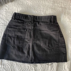 Svart jeanskjol - Säljer en svart jeanskjol med klassiska fickor fram och bak samt hällor för bälte. Kjolen har en rå, avklippt kant nedtill för en cool look. 💕
