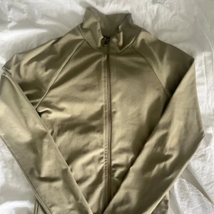 Grön/grå zip-jacka från Nelly - Säljer en grön/grå jacka från Nelly med dragkedja framtill och hög krage. Jackan har lång ärm och en tight passform som sitter snyggt på kroppen. Perfekt att ha på gymmet eller annan form av träning. (2 sista bilderna visar färgen bäst, konstigt ljus på första) Kom privat för mer info eller om pris ska diskuteras!