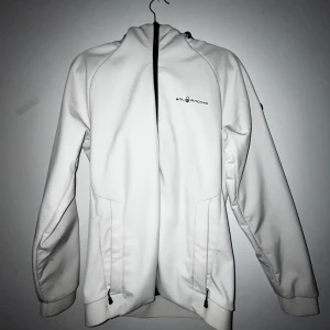 Vit softshelljacka från Sail Racing - Vit softshelljacka från Sail Racing med svart logga på bröstet och huva. Jackan har dragkedja framtill, två fickor med dragkedja och ribbade muddar. Perfekt för kyliga dagar och sportiga outfits. M men passar S också perfekt förbereddelse för hösten Pris är ej huggen i sten