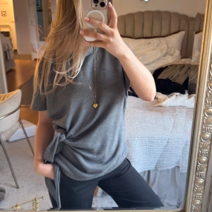 Grå t-shirt med knyt i sidan populär Zara  - Säljer en grå t-shirt med korta ärmar och snygg knytdetalj i sidan. T-shirten har en avslappnad passform och är perfekt för en chill vardagslook.  trendig. Storlek L men sitter såhär snyggt på mig som oftast är xs/s