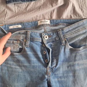 Ljusblå jeans från Jack & Jones - Säljer ett par ljusblå jeans från Jack & Jones med klassisk femficksdesign och knappar i gylfen. Jeansen har raka ben och är tillverkade i denim med snygga kontrastsömmar. Perfekta för en avslappnad stil.