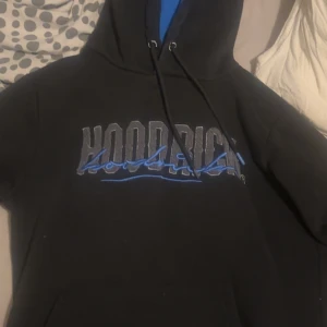 Svart hoodie från Hoodrich med blå detaljer - Säljer en svart hoodie från Hoodrich med blå och grå text på bröstet. Tröjan har huva med dragsko och en blå insida i luvan. Säljs inte längre, jätte bra skick!!!!