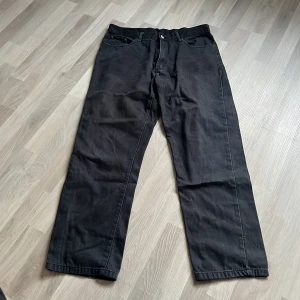 Svarta jeansbyxor från MC Gordon - Svarta raka jeansbyxor från MC Gordon i 100% bomull. Klassisk femficksmodell med knapp och dragkedja framtill. Snyggt diskret märke bak i midjan och etikett på insidan. Perfekta för en stilren och enkel look. Storlek 36/32