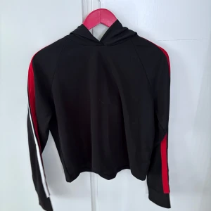 Svart hoodie med röda och vita detaljer från FB Sister - Säljer en svart hoodie från FB Sister i storlek XL. Tröjan har röda och vita ränder längs ärmarna och en huva. Perfekt för en avslappnad stil och enkel att matcha med jeans eller leggings.