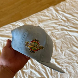 Ljusblå keps med broderad logga - Snygg ljusblå keps med broderad text och logga på sidan samt ett stort broderat R framtill. Justerbar snapback baktill för perfekt passform. Perfekt accessoar för en avslappnad stil.
