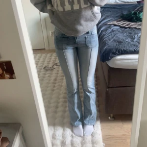 Ljusblå bootcut jeans från MADLADY - Säljer ett par ljusblå jeans med bootcut passform och markerade sömmar längs benen. Jeansen har stora fickor framtill och klassiska bakfickor med lock och knapp. Jag är 170 och storlek 34💕 kontakta ifall du har frågor om storlek!