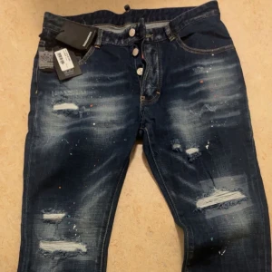 Dsquared2 Jeans - Säljer ett par mörkblå jeans från Dsquared2 med slitna detaljer och färgstänk. Byxorna har flera revor och en tvättad look som ger en cool och trendig stil. Passar dig som gillar streetwear och vill sticka ut. Pris kan diskuteras.