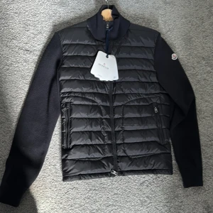 Moncler Wool Cardigan  - Snygg svart pufferjacka från Moncler med quiltad front och släta ärmar. Jackan har dragkedja framtill, ståkrage och två fickor med dragkedja. Perfekt för kyliga dagar och stilren look. Helt ny och oanvänd, tags är kvar. Nfc funkar.