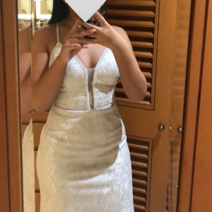 Glittrig vitsilvrig långklänning med mermaidform - Säljer en vitsilvrig långklänning med glittrigt tyg och spetsdetaljer. Klänningen har smala axelband, djup v-ringning och markerad midja. Perfekt för bal eller bröllop. Dragkedja och snörning i ryggen med lätt utställd kjol. Klänningen har använts en gång. Strl S/38.  Nypris 2500. 