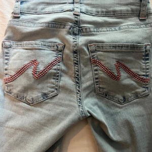 Ljusblå jeans - Ljusblå jeans från Nelly med rosa brodering på fickorna och hål vid knäna.  Jättefina i väldigt bra skick endast lite slitningar längst ner i bak på ena benet,se bild ovanför. Skriv för fler bilder eller frågor.