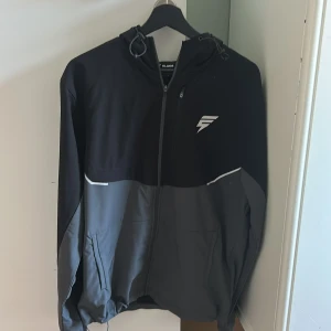 Svart och grå vindjacka från Slude - Säljer en svart/grå track jacket från Elude , ny skick , storlek M , Reflex detaljer , ficka på ryggen kan justera luvan och midjan , vind material. Perfekt för träning eller bara till vardagen . Pris kan diskuteras 