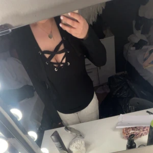 Svart långärmad topp med snörning - Svart långärmad topp med djup v-ringning och snörningsdetalj framtill. Snygg och trendig modell som passar perfekt till både jeans och kjol. Mjuk och stretchig i materialet.  