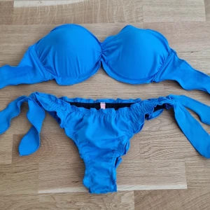Blå bikini med knytband - Säljer en klarblå bikini med vadderad bygel-bh och knytband i ryggen. Knyts även i sidorna på bikinitrosor. Storlek S i bhn och XS i trosan.