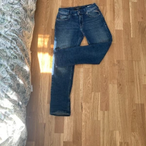 Blå jeans från Replay Wallys - Säljer ett par klassiska blå jeans från Replay, modell Wallys. Jeansen har fem fickor, raka ben och snygga slitningar för en cool look. Perfekta till vardags och passar till det mesta. Märkesdetalj på fickan och knappstängning.
