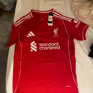 Liverpool tröja  - Har äntligen fått tag på  Liverpools nya hemma tröja  från Adidas med vita detaljer och tryck. Nummer 7 och Luis Díaz på ryggen. Standard Chartered sponsortryck på bröstet och LFC-logga. Tröjan är Slim fit kom gärna med förslag vi kan diskutera fram ett bra pris 