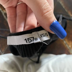 Svart ribbad linnetopp från 157 - Säljer en svart ribbad linnetopp från 157 med tunna axelband och rak halsringning. Toppen är tight och har en enkel, stilren design som passar perfekt till sommaren.