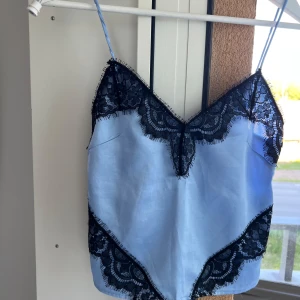 Ljusblå linnetopp med svarta spetsdetaljer - Supersöt ljusblå linnetopp med tunna axelband och svarta spetsdetaljer. 