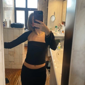 Svart offshoulder topp - Säljer en svart offshoulder topp med långa ärmar. Toppen är tight och croppad, perfekt för en trendig look. Enkel och stilren design utan synliga mönster eller detaljer.