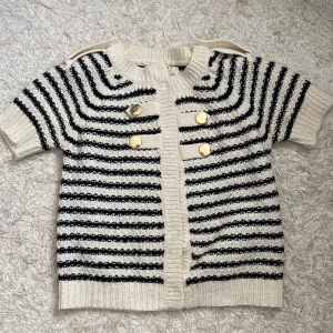 Randig stickad kofta med guldknappar från River Island - Säljer en krämvit och svart randig stickad kofta. Koftan har korta ärmar och dekorativa guldknappar framtill. 