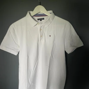 Vit pikétröja från Tommy Hilfiger i toppskick - Klassisk vit pikétröja från Tommy Hilfiger. Tröjan har en liten broderad logga på bröstet och är tillverkad i bomull. Perfekt för sommaren, endast använd 1 gång. Storlek 176 men passar mig som bär storlek S. Som ny.
