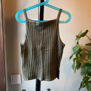 Olivgrön ribbad linnetopp - Snygg olivgrön ribbad linnetopp med raka axelband och croppad passform. Perfekt att matcha med jeans eller kjol för en trendig look.