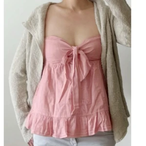 Rosa linnetopp med rosett och volang - Y2K! Supersöt rosa linnetopp med smala axelband, stor rosett framtill och volangkant nedtill. Perfekt för varma dagar och ger en romantisk känsla till outfiten. Lätt och luftig i materialet, köpt i USA, går inte att få tag på längre! Helt oanvänd så i nyskick. Storlek XS, passar också S. Priset går inte att diskutera. Använd gärna KÖP NU om du vill köpa.