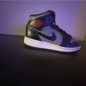Nike Air Jordans i svart och grått - Säljer ett par Nike Air Jordans med svart och grå ovandel, klassisk röd logga vid ankeln och vit sula. Skorna har snörning och rund tå, perfekt för dig som gillar streetwear och sneakers med ikonisk design.