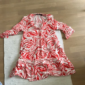 Rödvit mönstrad klänning från Vero Moda - Säljer en färgstark klänning från Vero Moda i rödvitt mönster. Klänningen har trekvartsärm, v-ringning och volangdetaljer nertill. Perfekt för dig som gillar unika mönster och bekväm passform.