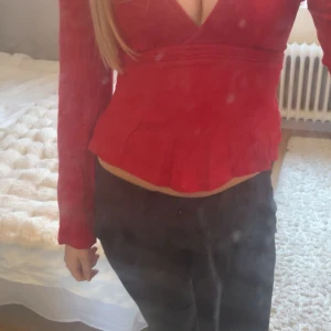 Röd topp med knyt i ryggen från Gina  - Säljer en röd topp med långa ärmar och v-ringning. Toppen har en fin volangkant nedtill och knytband i midjan som ger en snygg siluett. Perfekt för dig som vill ha en färgstark och trendig look. Säljer för jag inte använder ❤️