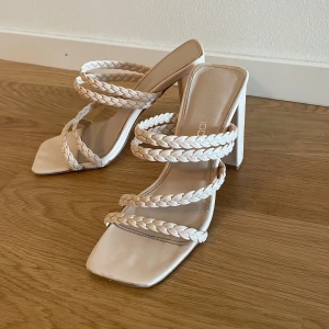 Beiga sandaler med flätade remmar och klack - Säljer ett par trendiga beiga sandaler med fyrkantig tå och höga blockklackar. Skorna har tre flätade remmar över foten som ger en snygg och modern look. Perfekta för att lyfta din outfit!