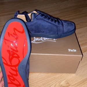 Blå sneakers från Christian Louboutin - Säljer ett par exklusiva blå sneakers från Christian Louboutin i mocka med den ikoniska röda sulan. Skorna har snörning och rund tå, samt broderad logga på hälen. Perfekta för dig som vill sticka ut med stil. Box, bag och allt följer med!