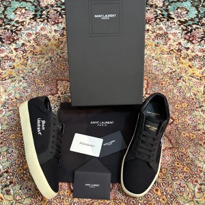 Svarta sneakers från Saint Laurent - Säljer ett par helt nya svarta Saint Laurent sneakers. Tydlig logga på sidan. Skorna har rund tå, platt sula och är tillverkade i textil och syntetmaterial. Klassisk och stilren design med svarta skosnören och diskreta detaljer.
