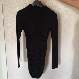 Svart långärmad tight klänning med rynkade detaljer - Säljer en svart långärmad klänning med tight passform. Klänningen har en hög hals och är tillverkad i ett stretchigt material som sitter snyggt på kroppen. Den är i storlek m men passar xs och s också 💕