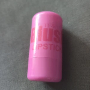 Blush Lipstick i mörklila nyans - Säljer ett läppstift från Blush i en mörkbrun nyans. Hylsan är rosa och kompakt, perfekt att ha med i väskan. Läppstiftet har en klassisk rund form och ger en intensiv färg till läpparna. Kan användas till både lappar och kinder.